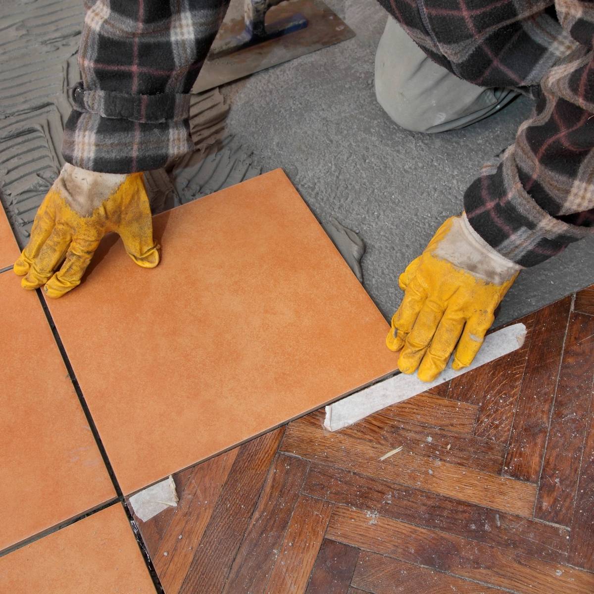 Person installing ceramic floor tiles over wooden parquet.