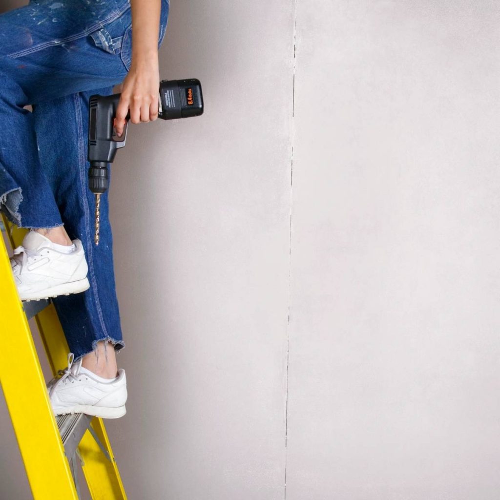 Person on ladder holding a power drill.