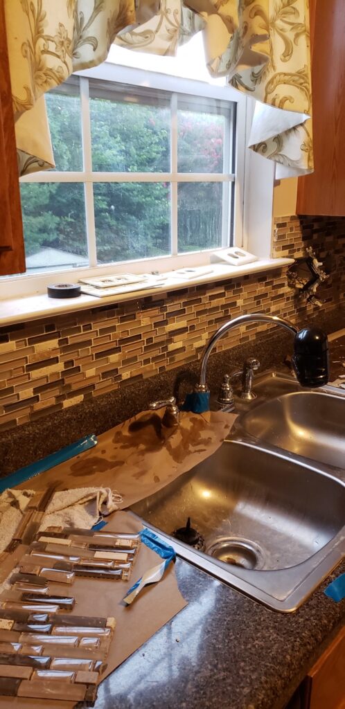 Kitchen countertop and sink with tile backsplash and window.