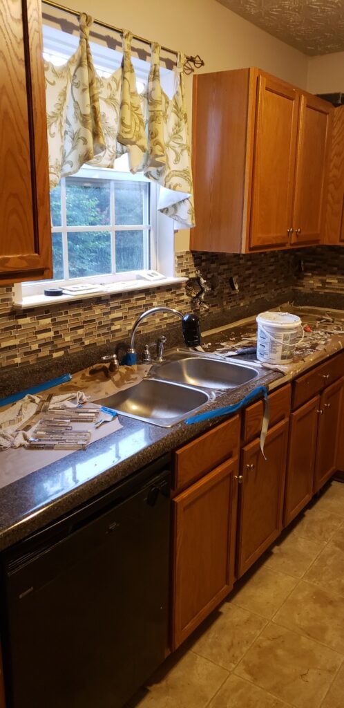 Kitchen sink area with wooden cabinets and backsplash under a window.