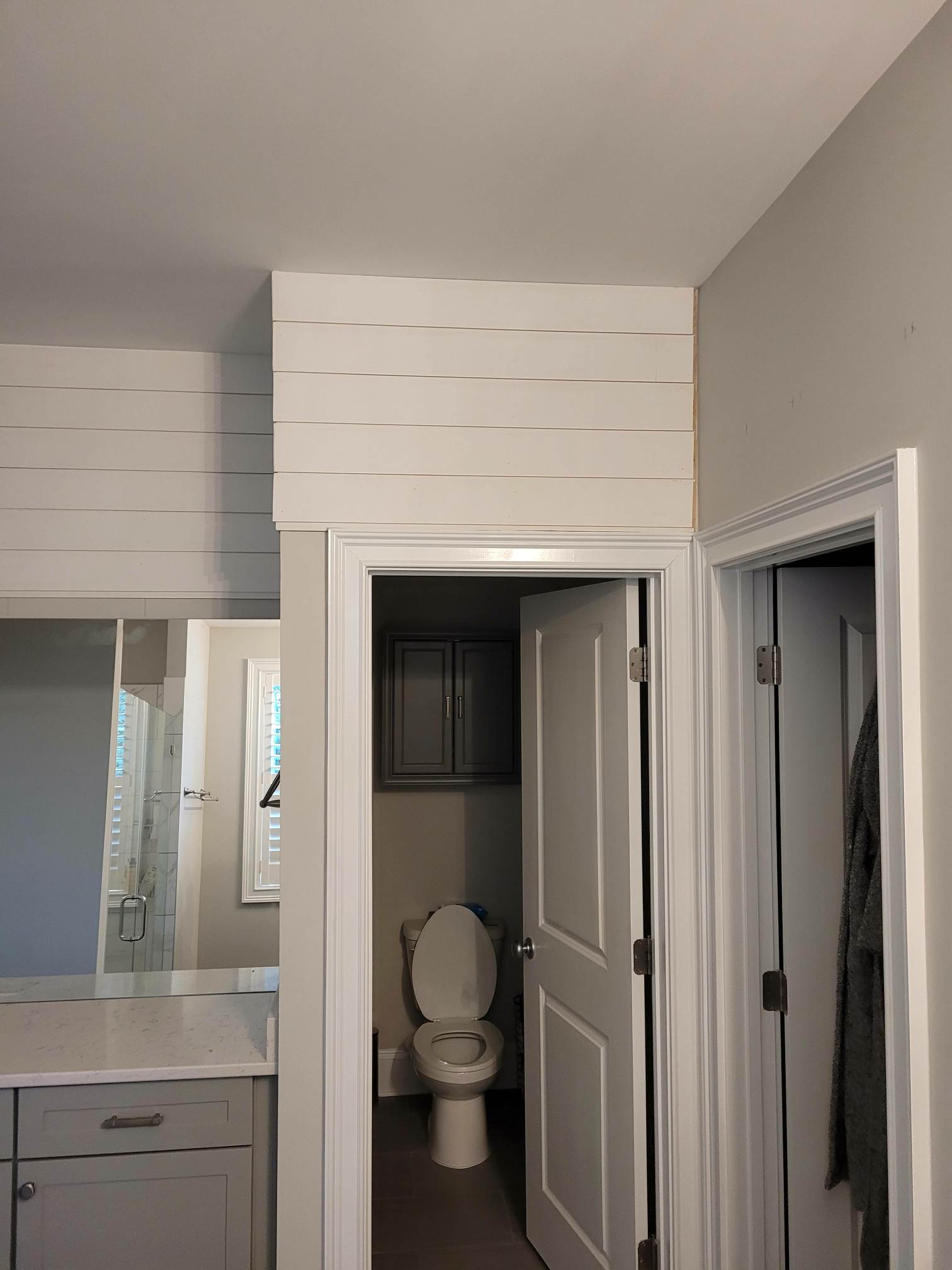 Bathroom with open door and upper storage cabinets.