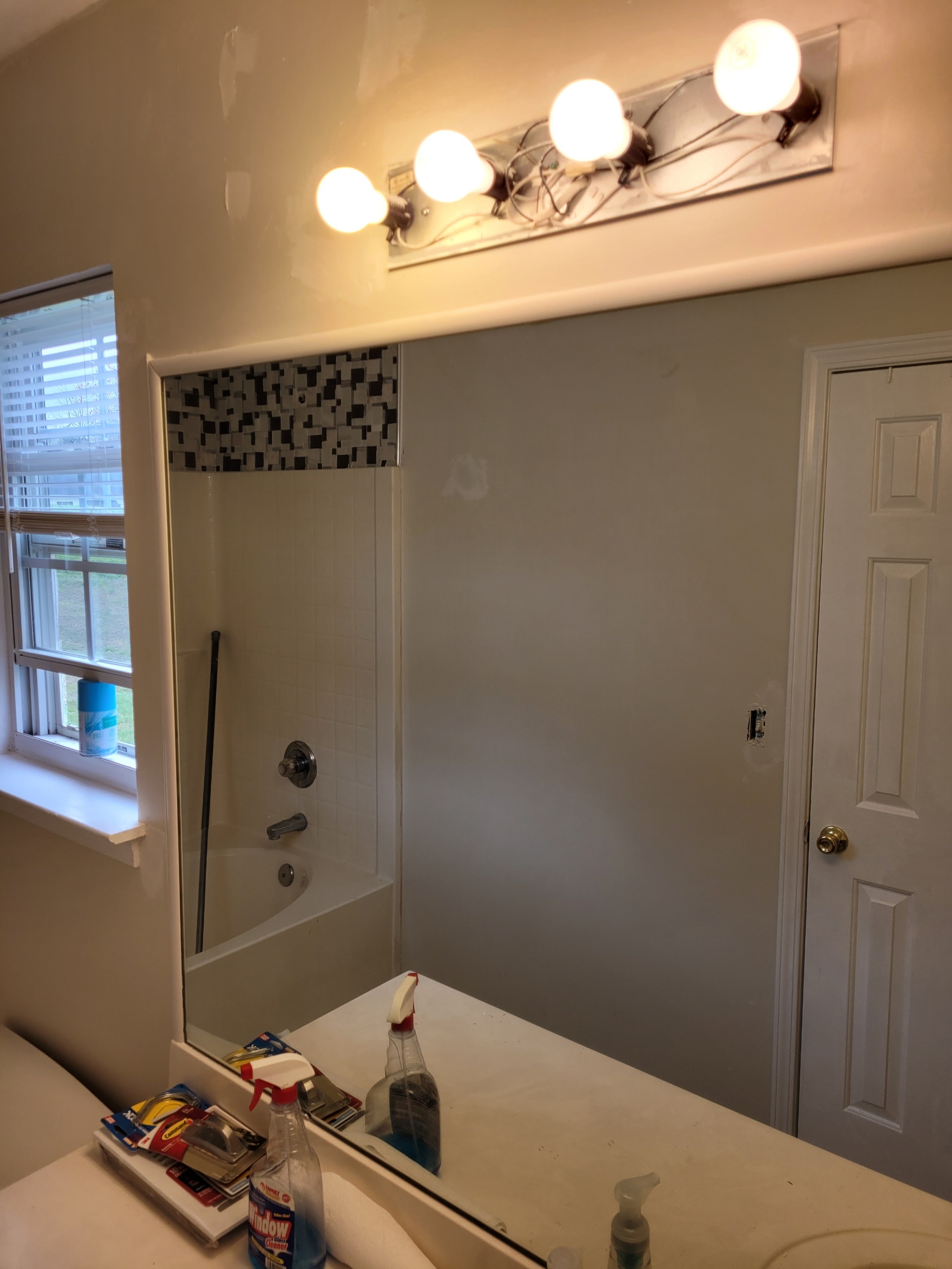 Bathroom mirror reflecting a bathtub, window, and door with light fixtures above.