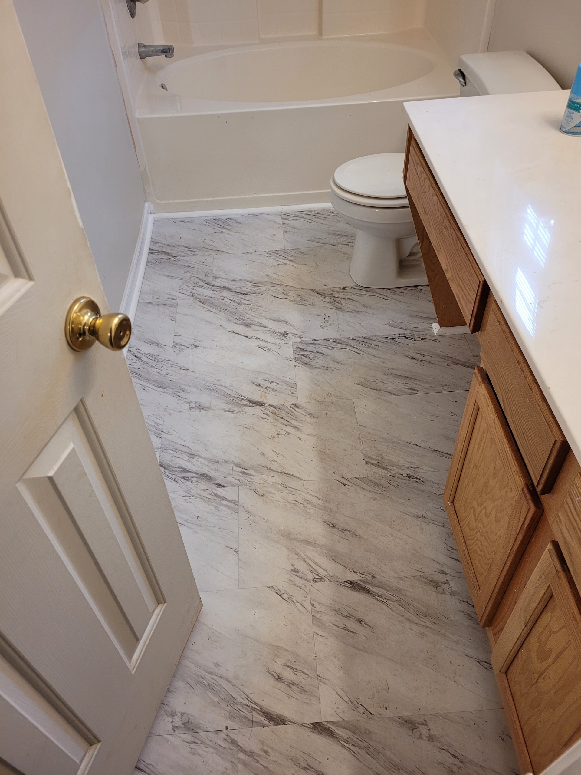 A bathroom with marble-patterned floor tiles, a wooden vanity, and a white toilet.