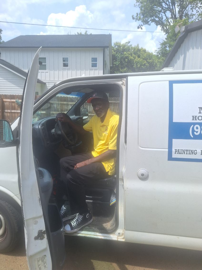 A person in a yellow shirt sitting in the driver's seat of a white van with the door open.