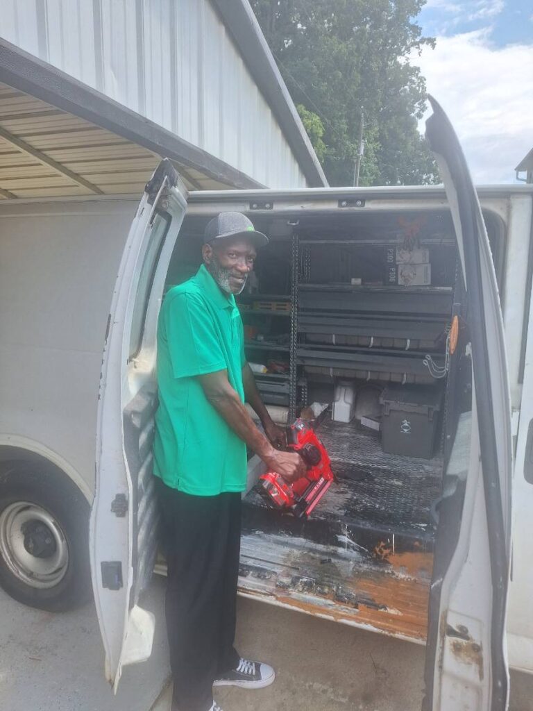 Man unloading equipment from a van, holding a red tool.