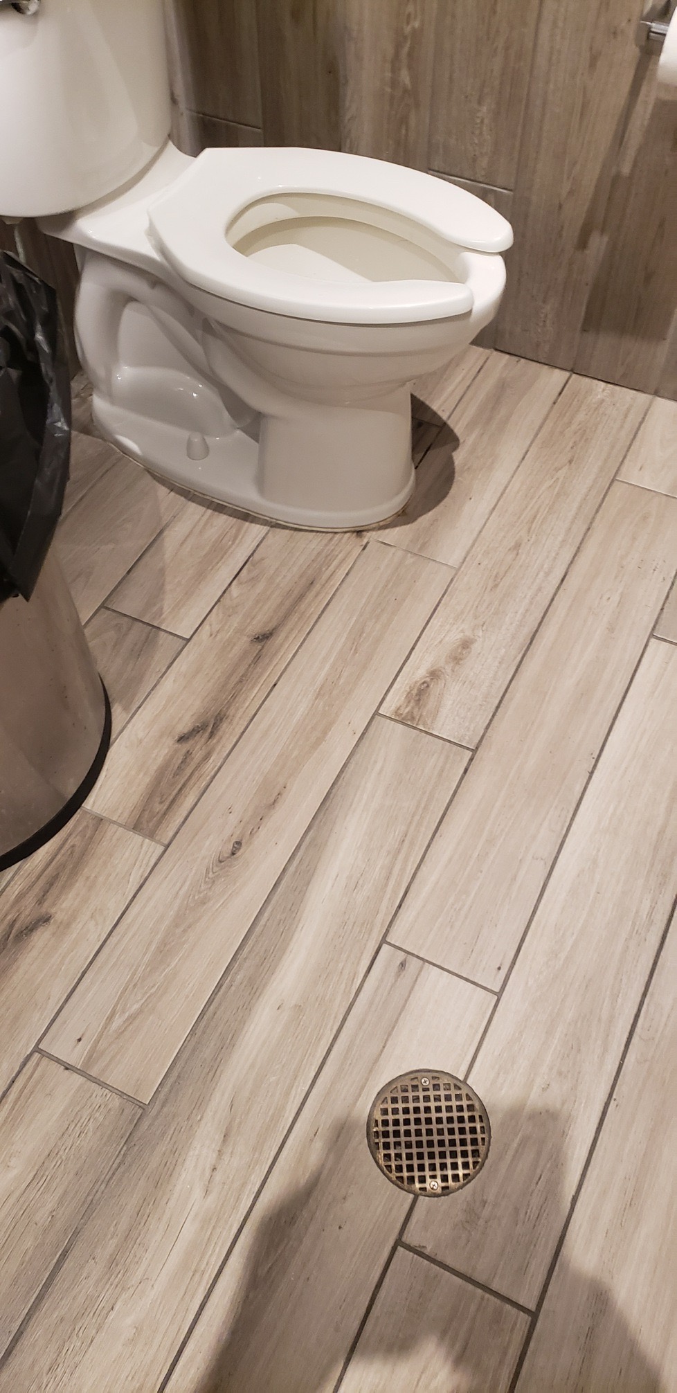 Close-up of light wood-patterned floor tiles with subtle cracks and a trash bin.