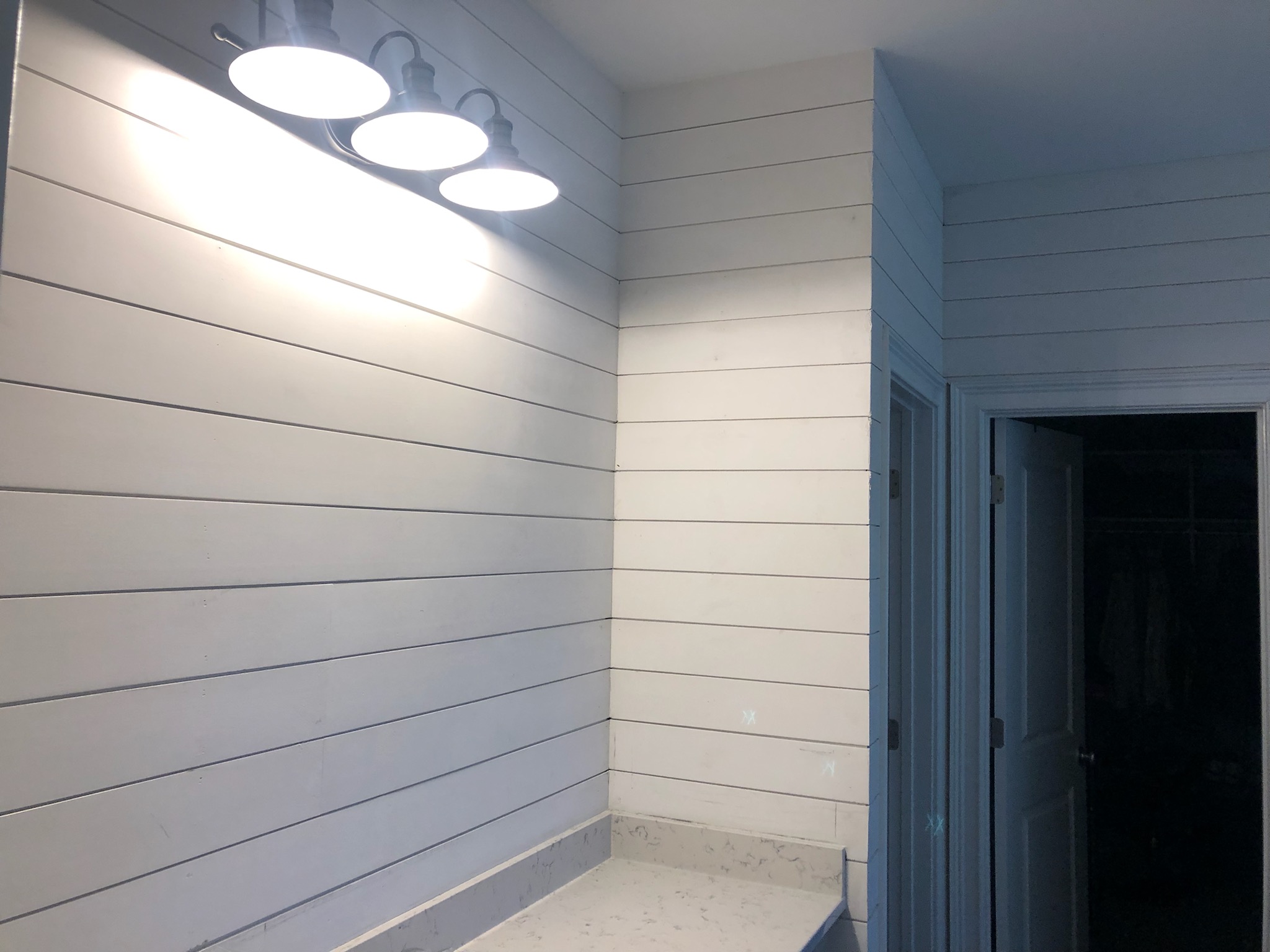 A modern bathroom corner with white shiplap walls and bright overhead lights.