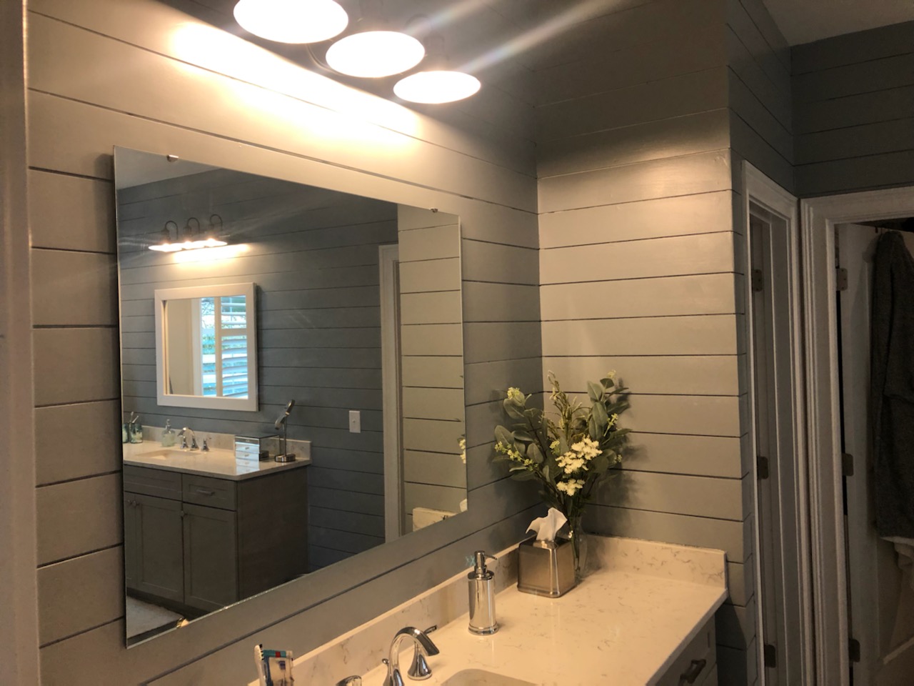 Modern bathroom with large mirror and elegant lighting.