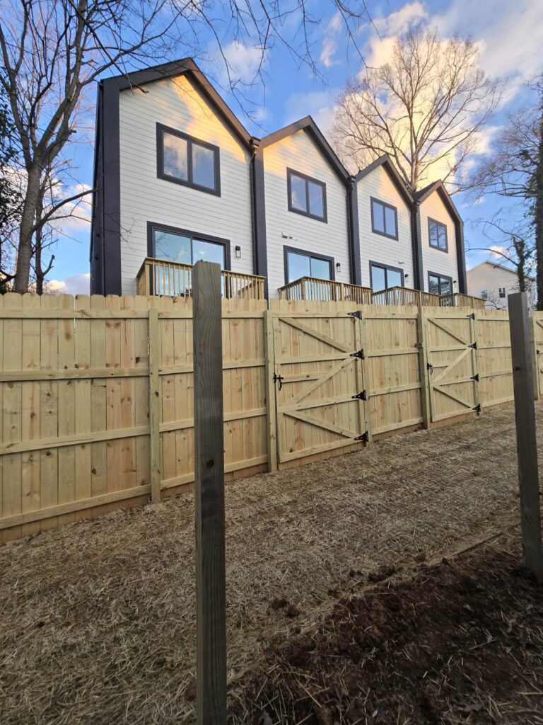 Newly installed wooden fence panels in a residential backyard under bright evening light.